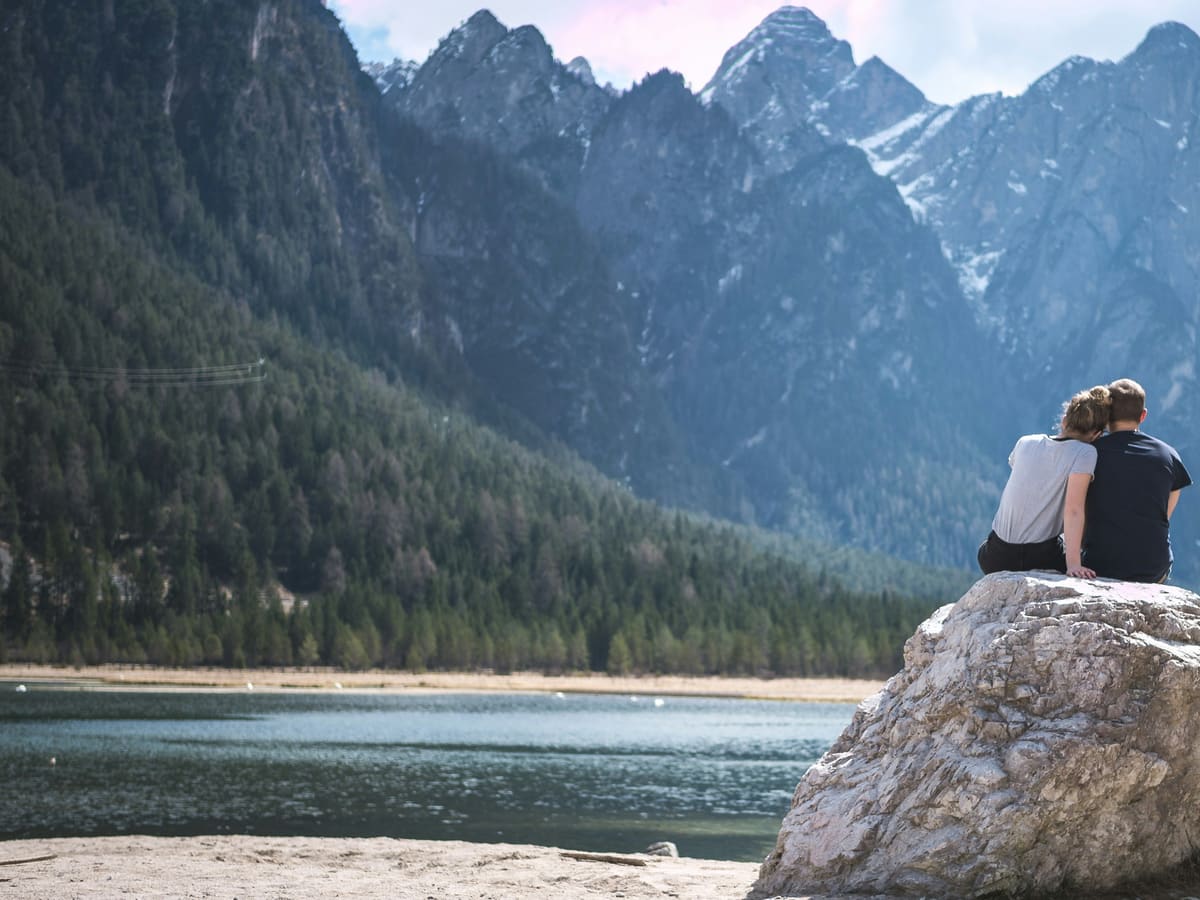 A couple sitting close together, looking out over a calm lake and mountains