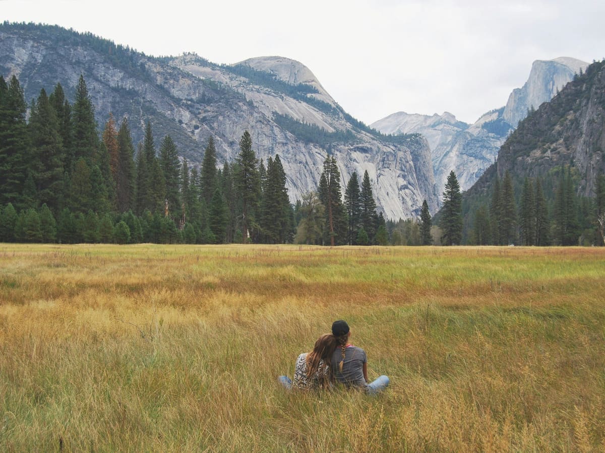 A couple sitting in a meadow, facing the mountains together